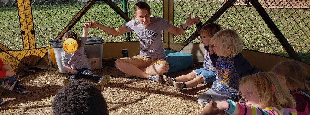 Children sitting in a circle with their teacher outside